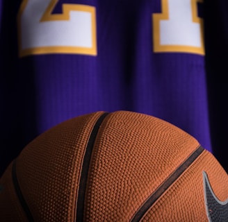 A close-up view of a textured basketball positioned in front of a purple sports jersey with the number 24 in white and yellow.