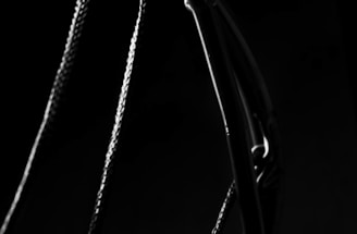 A close-up view of a basketball hoop is depicted, emphasizing its metal rim and the woven netting against a dark background. The lighting creates a dramatic contrast, highlighting the texture of the net and the sleekness of the rim.